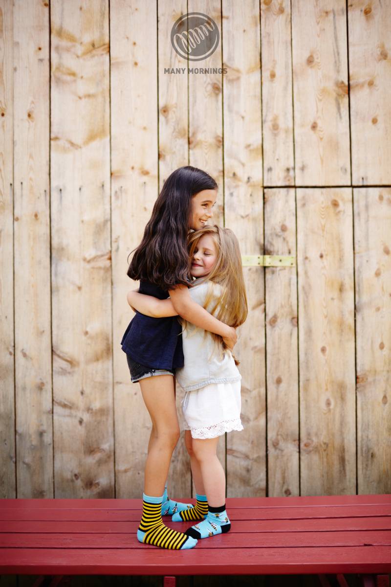 Dwie dziewczynki przytulają się. Na stopach mają kolorowe skarpetki w pszczoły.