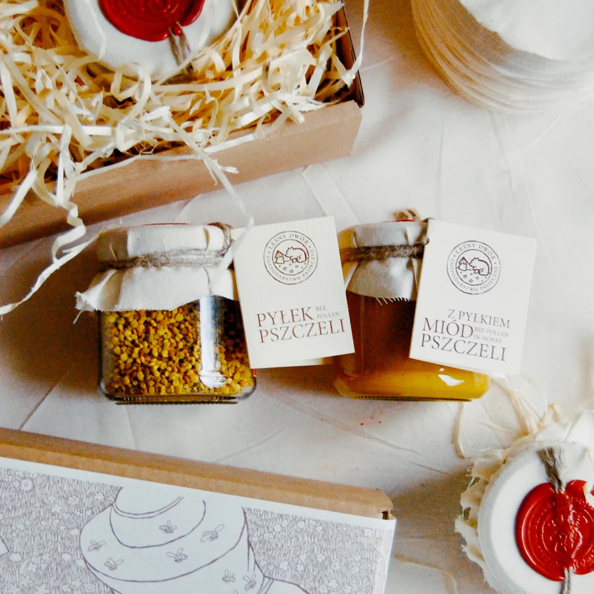 Wypakowane z pudełka prezentowego pyłek pszczeli i miód z pyłkiem. Wokół słoików ekologiczne pudełko prezentowe z papierową obwolutą.